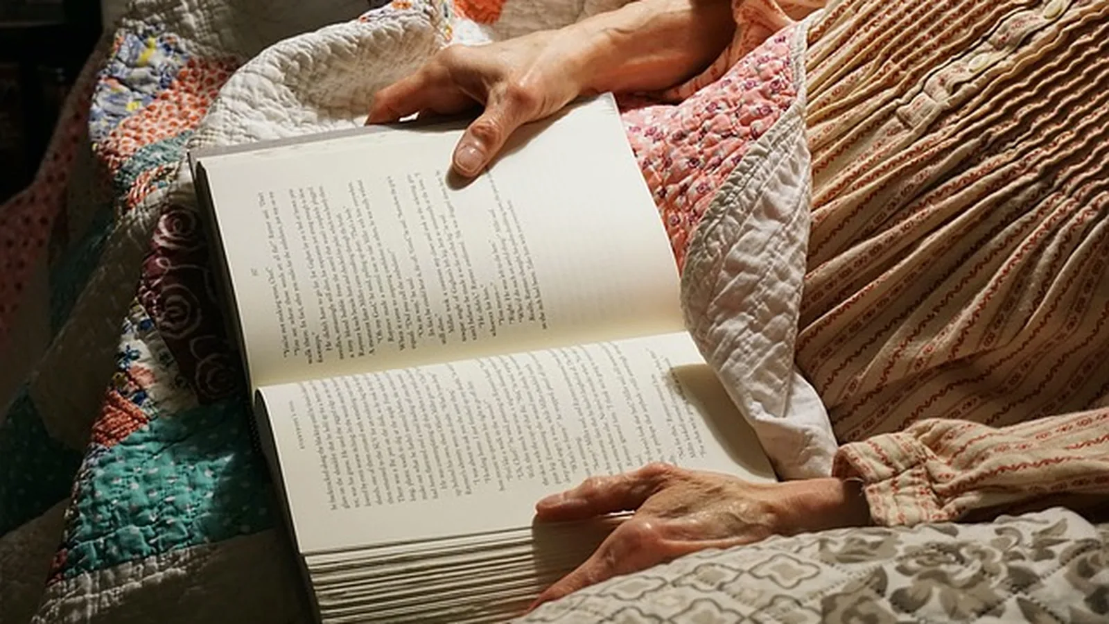 Close-up of an older adult's hands turning the pages of a book while reading at home